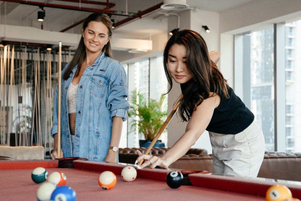Two woman smiling and playing billiards in their new rec and game room.