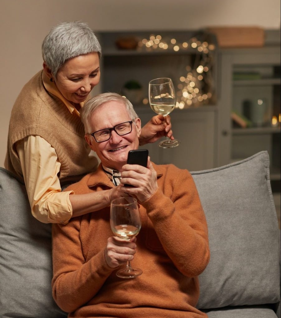 Middle-aged couple smiling, drinking wine, and looking at husband's phone in their new wine room.